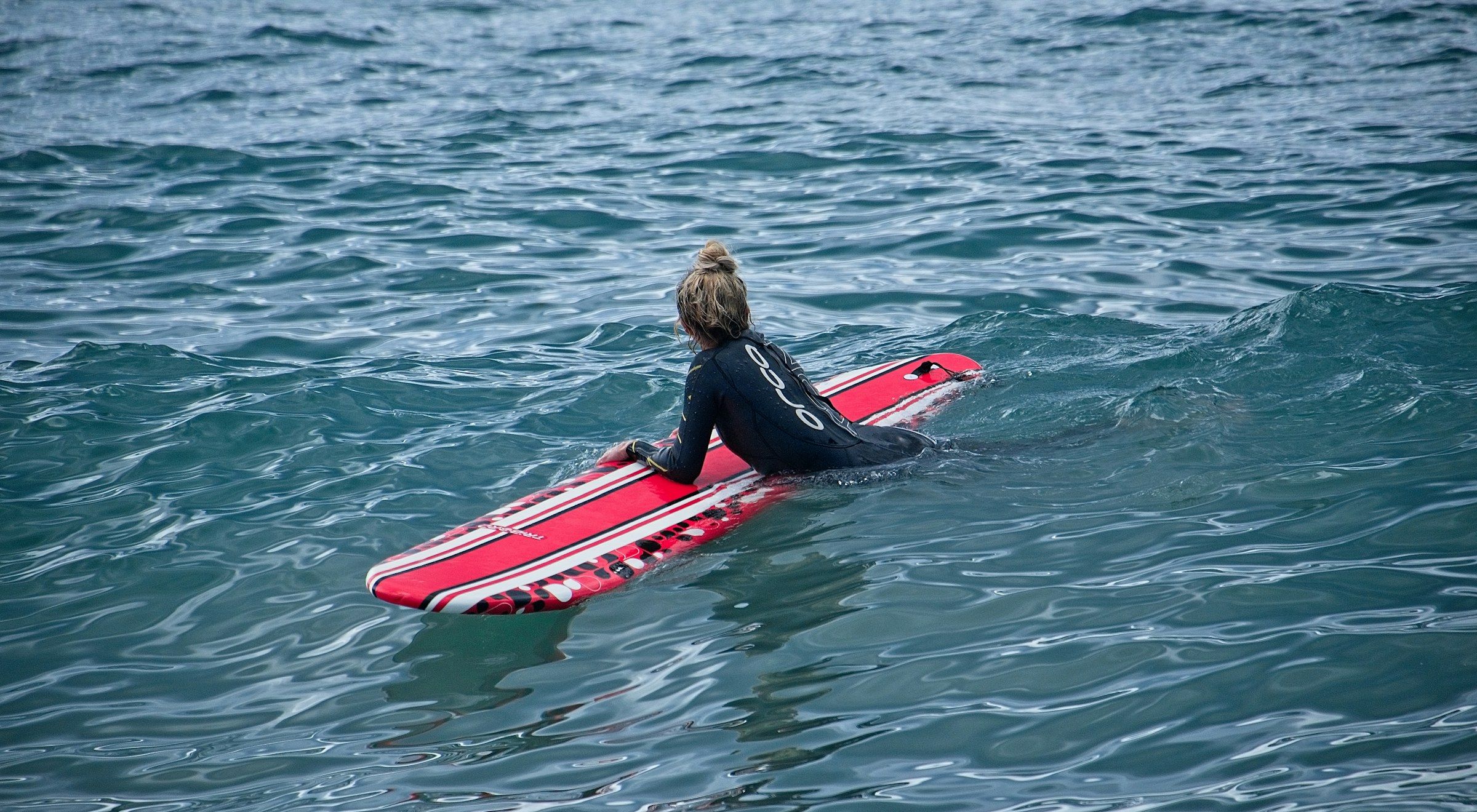 Une nageuse allongée sur une planche rouge rame dans les vagues