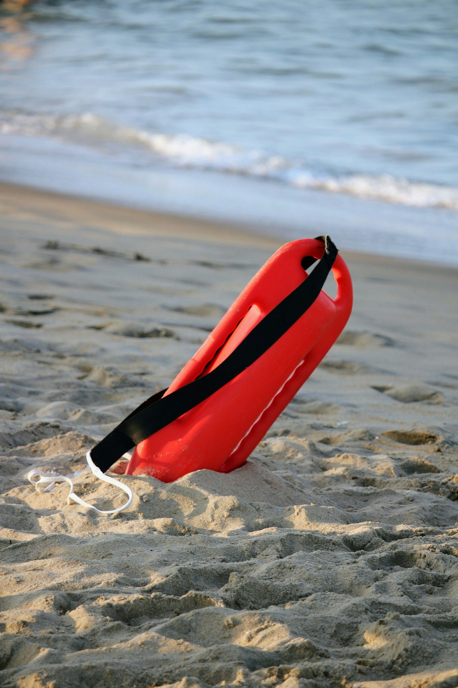 Une bouée tube rouge posée sur le sable, au bord de l'eau