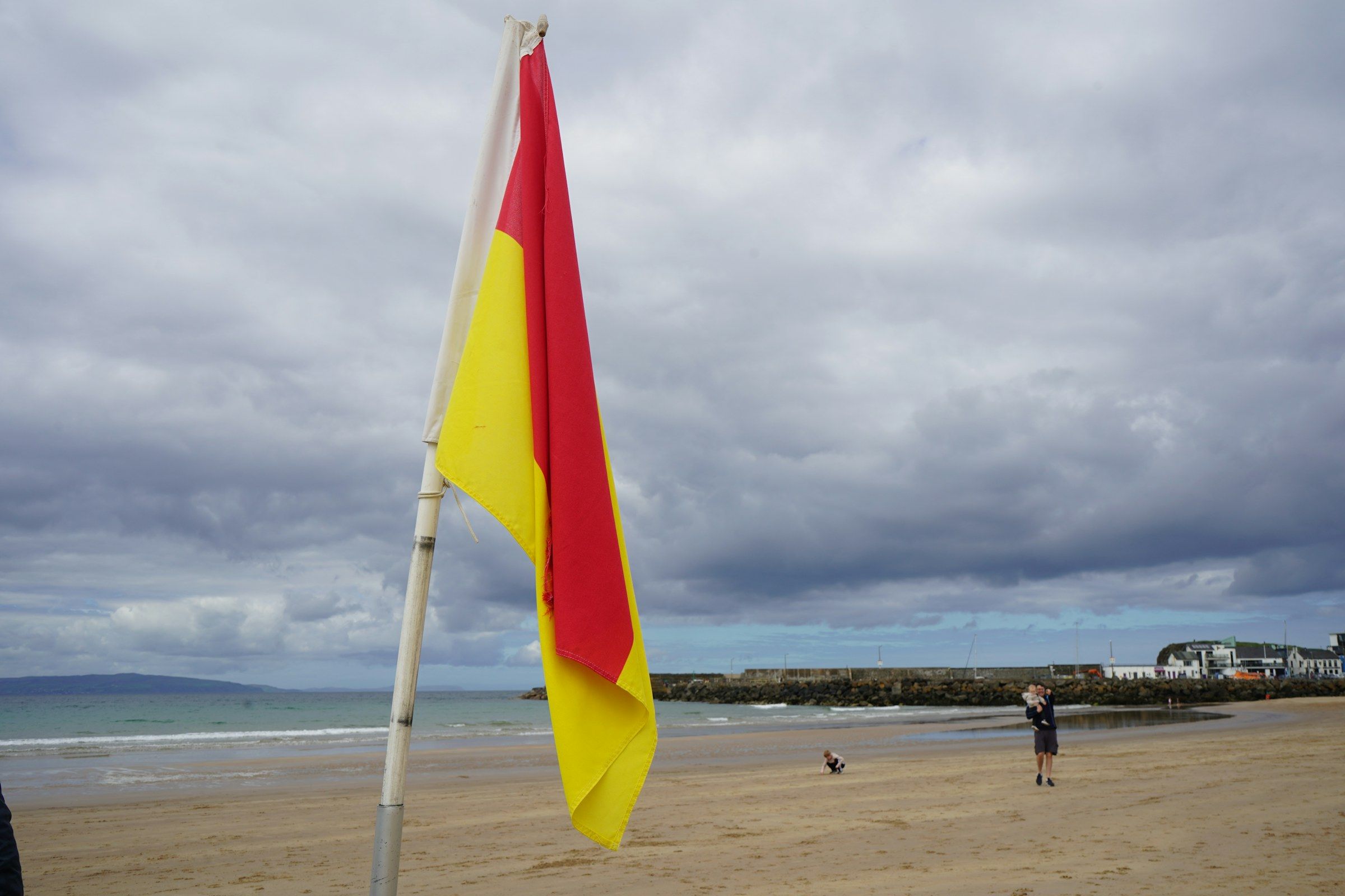 Drapeau rouge et jaune planté sur une plage sous un ciel nuageux